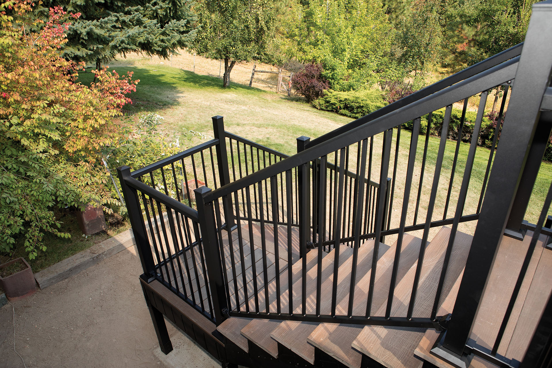 Multi-level deck stairs leading to backyard with trees and grass.