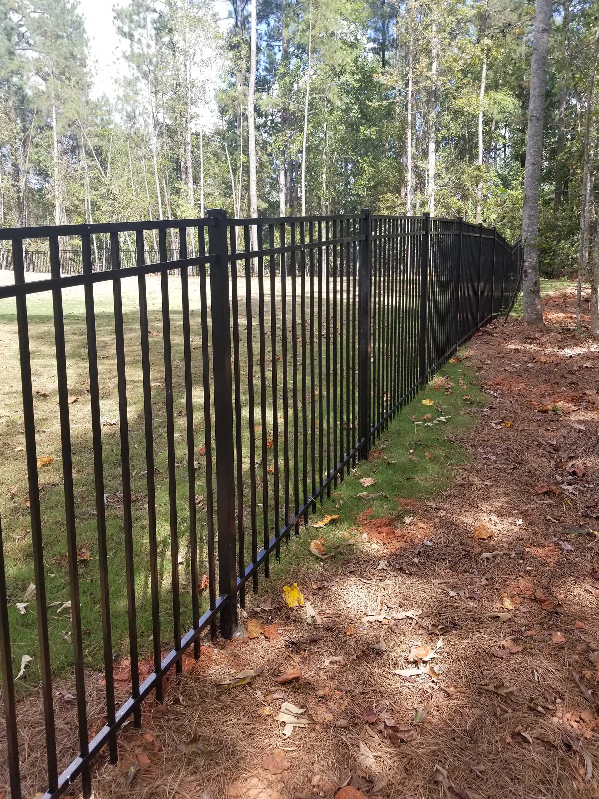 Aluminum fence following the slope of a forested backyard, demonstrating rackable panel technology.