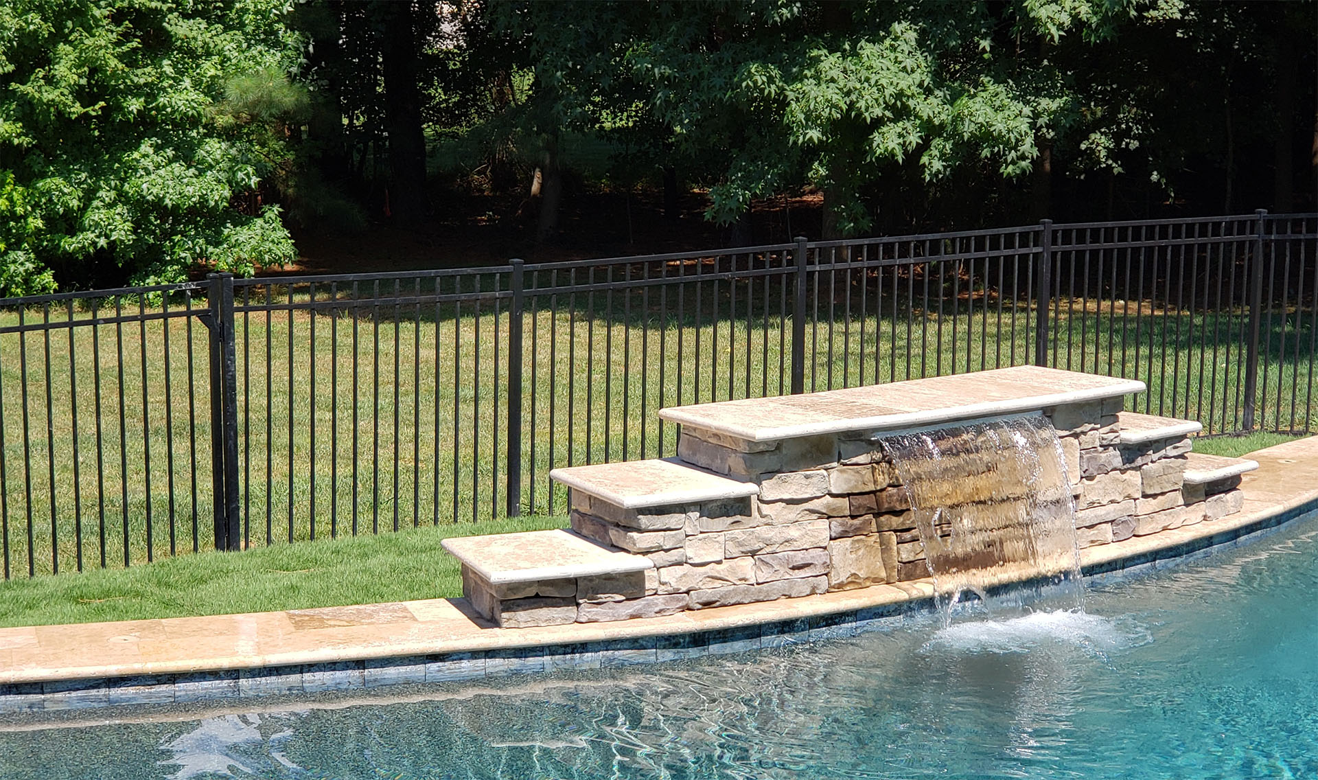 Black aluminum fencing installed around a backyard pool with waterfall feature.