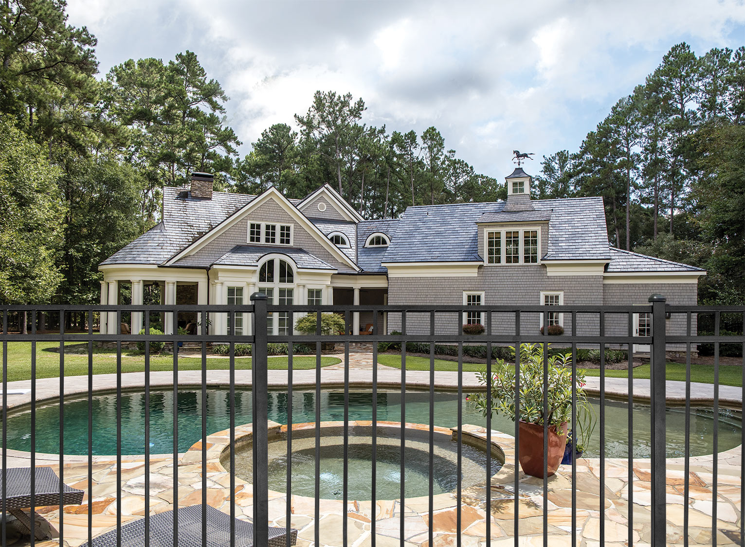 A residential steel fence surrounds a pool in front of a house, providing safety and privacy.