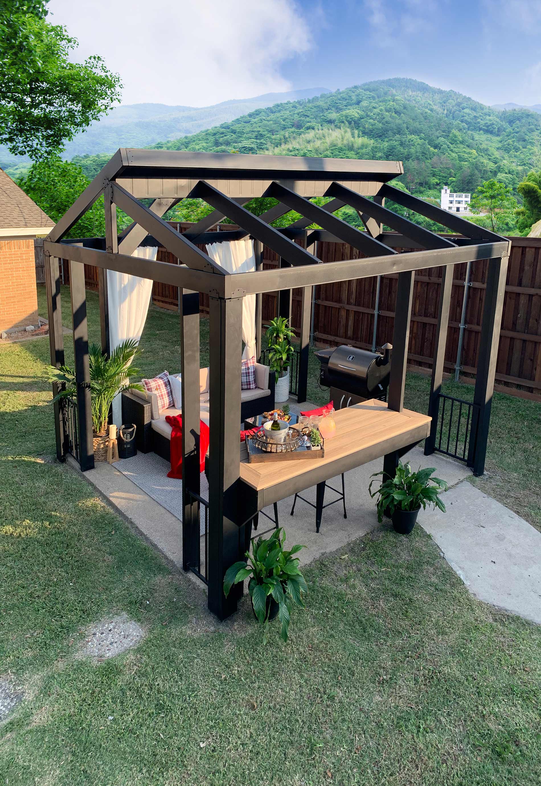 Overview of a steel pergola creating a living room outside with couches and a table for entertaining.