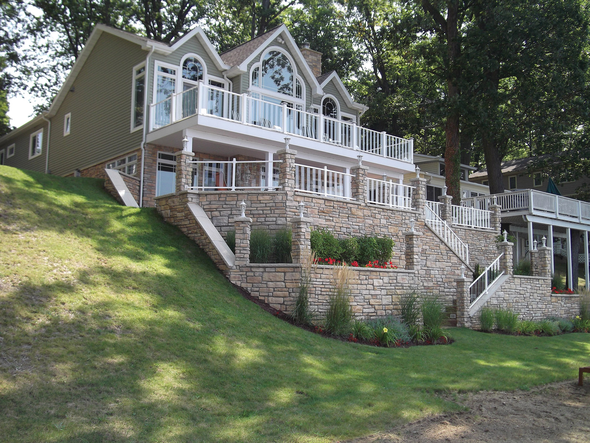 Modern outdoor deck with glass railings and lush greenery.