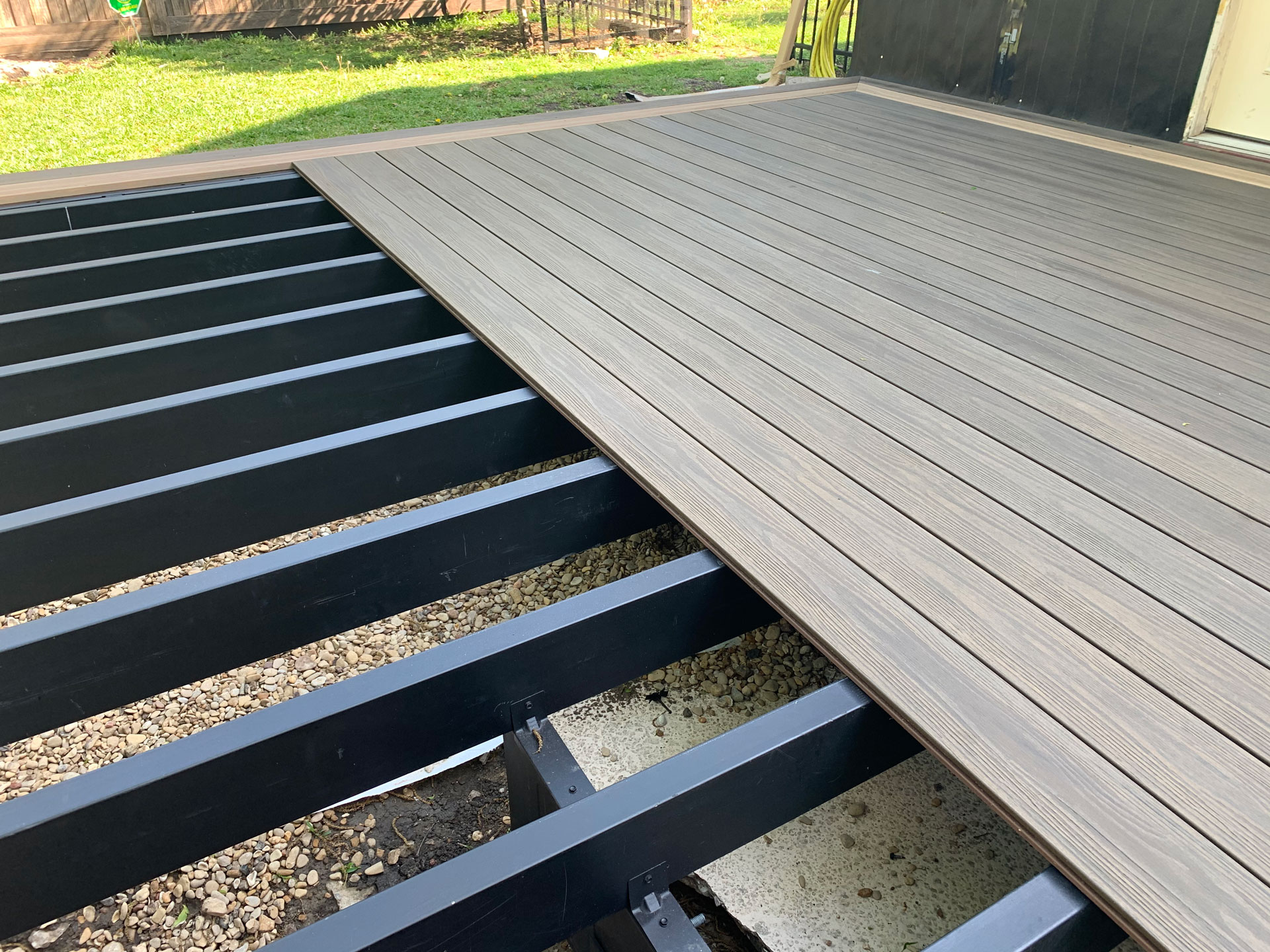 Half of a light colored deck installed on steel framing with yard in the background.