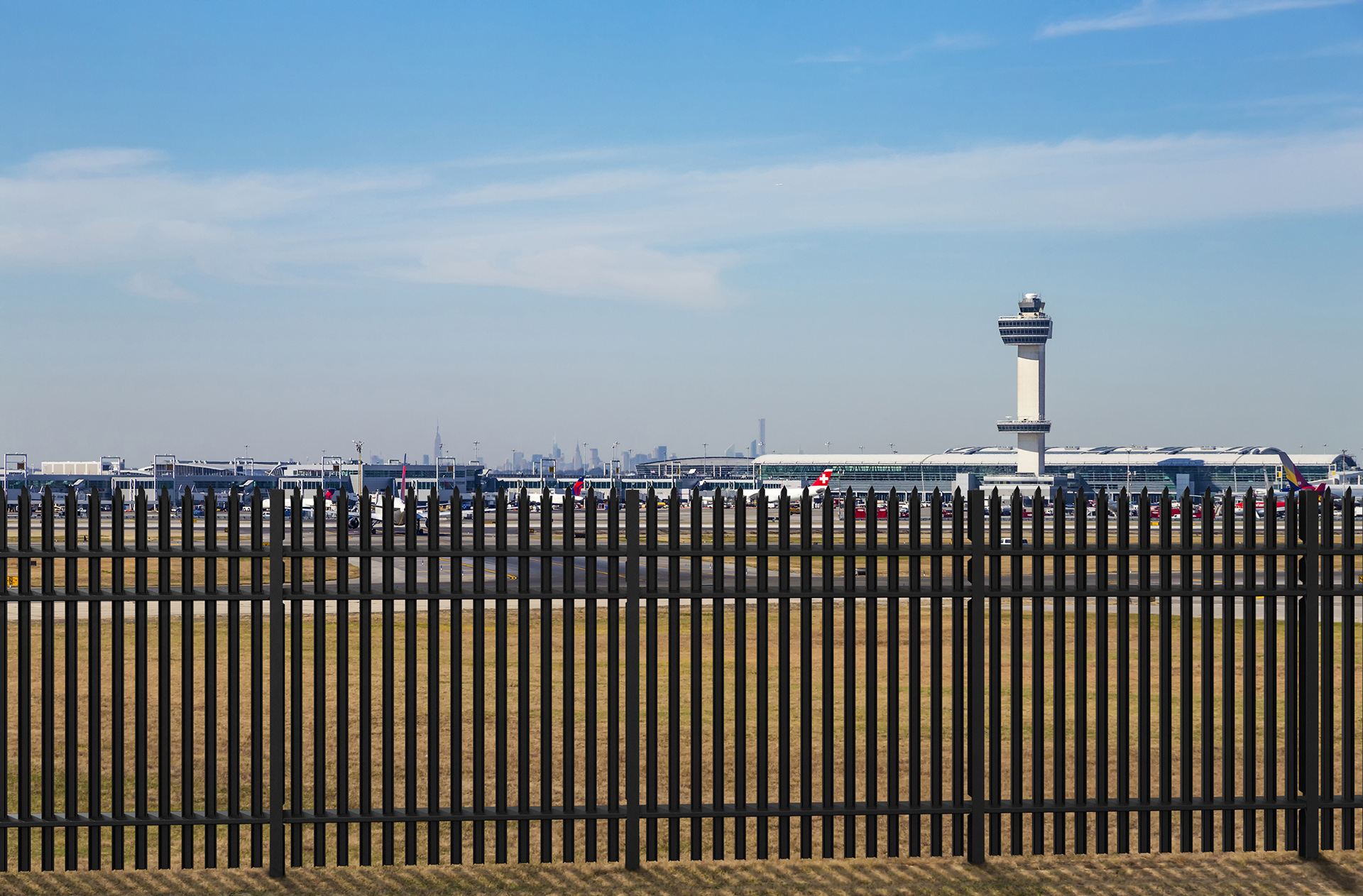 High-security steel perimeter fence securing an airport with control tower in the background.