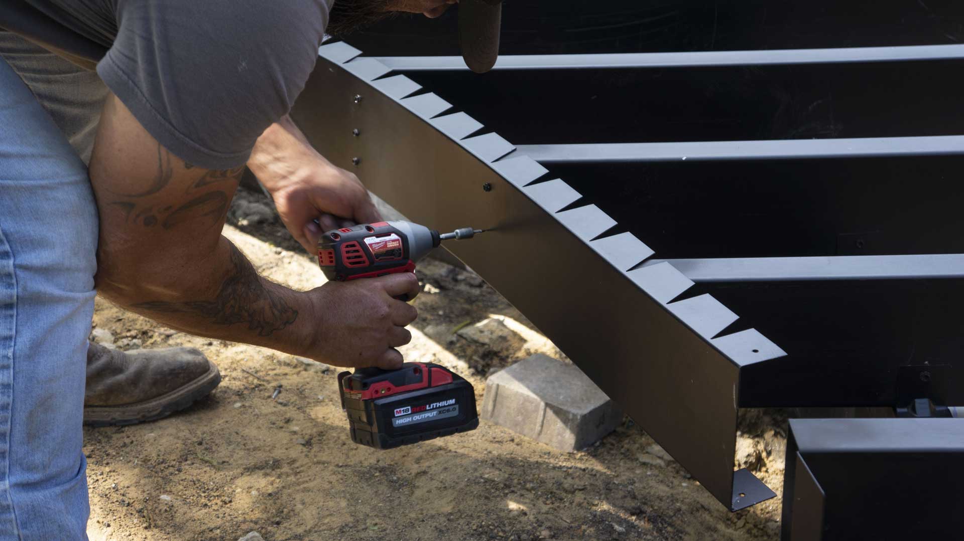 Close-up of a worker using a power drill to secure a steel deck frame.