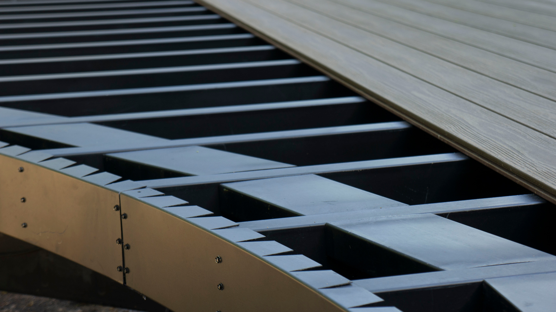Black curved steel deck framing with decking being installed on top.