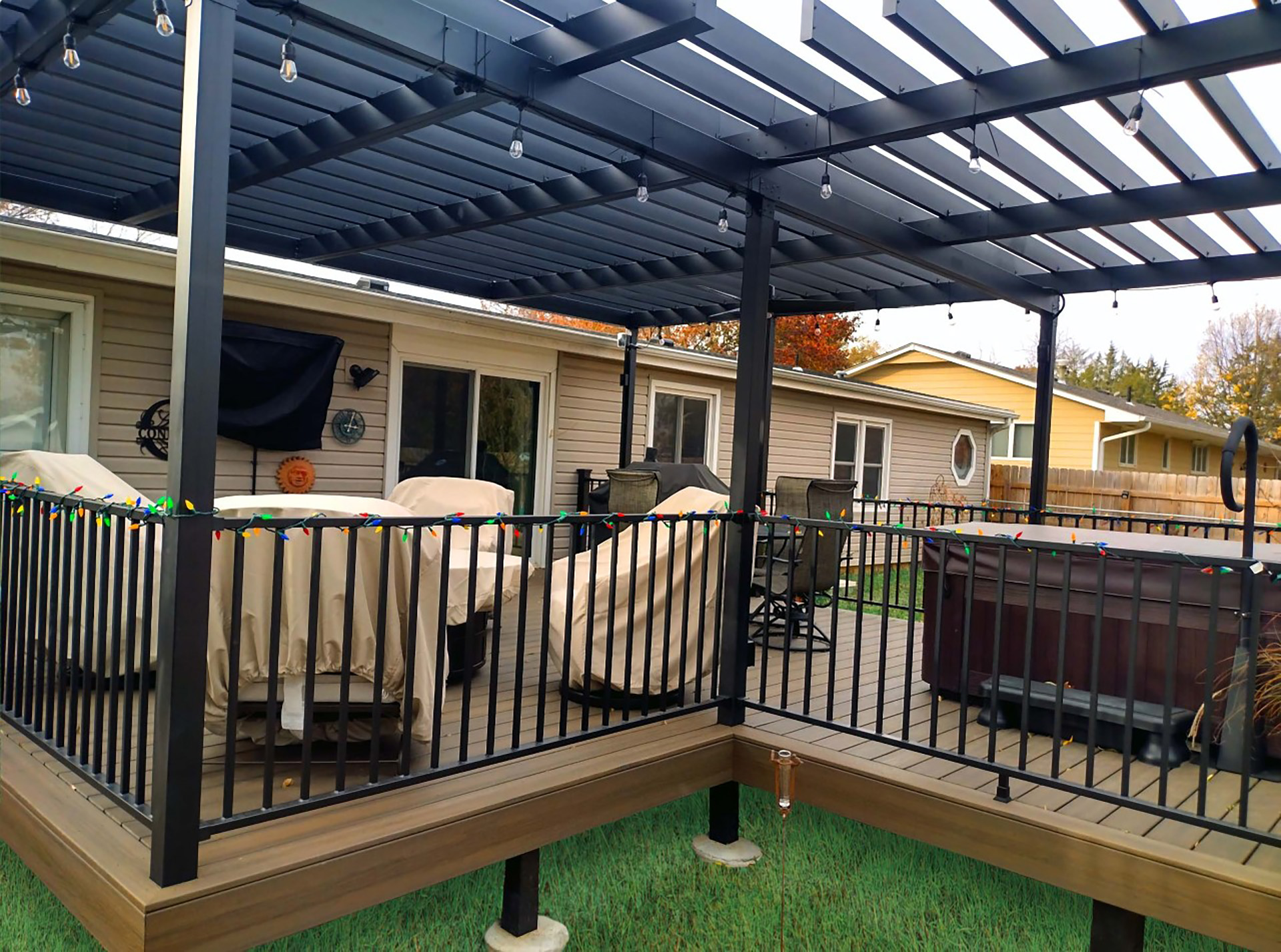 Steel pergola installed on backyard deck with string lighting and railing.