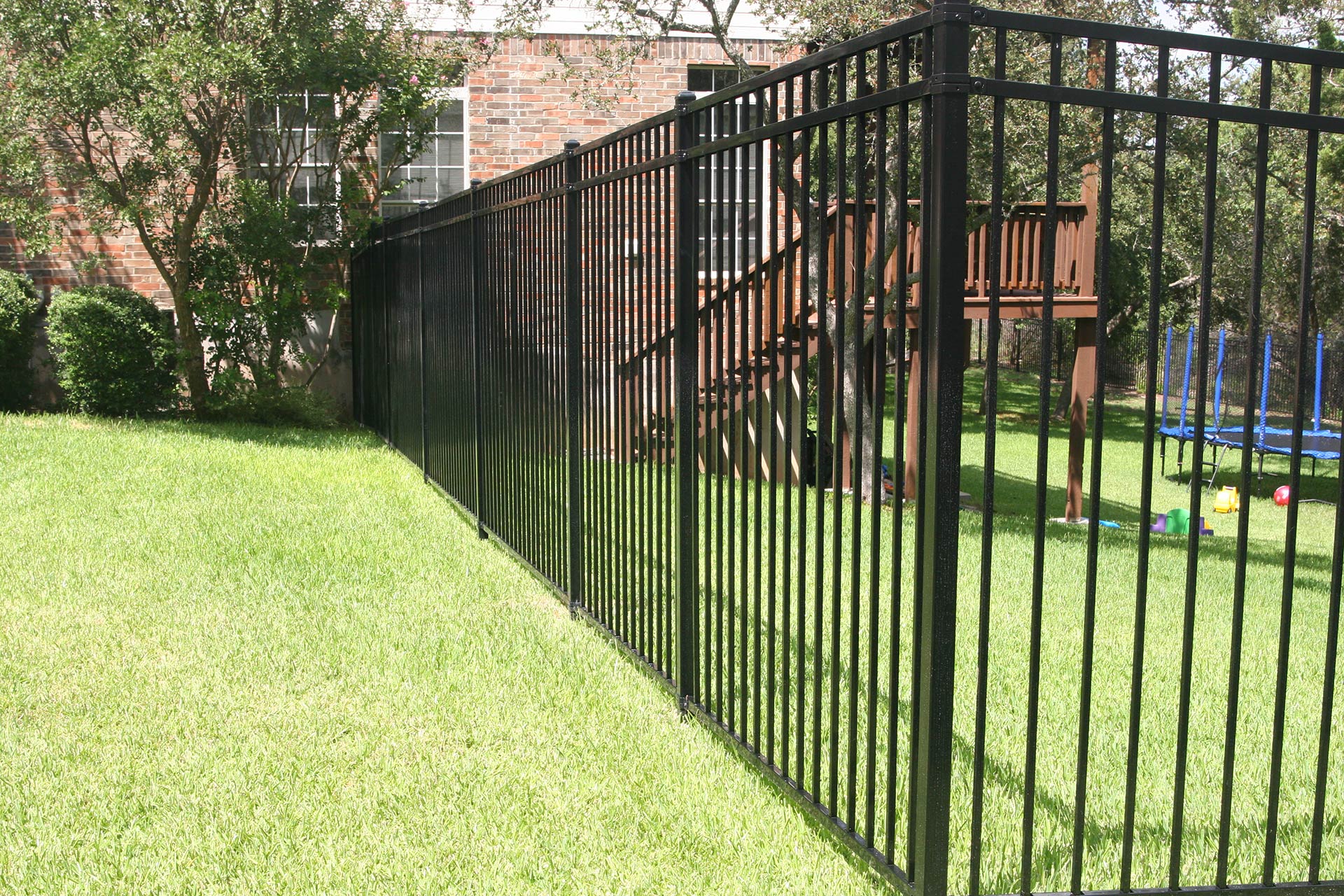 A durable black steel fence surrounding a backyard with a playground.